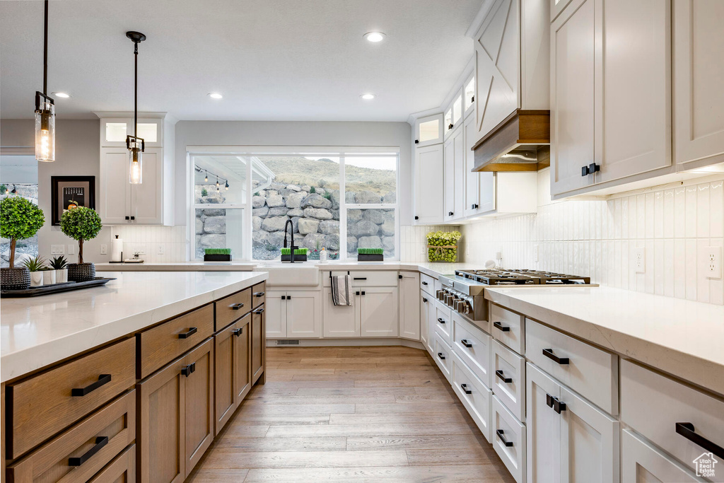 Kitchen featuring tasteful backsplash, custom range hood, white cabinetry, light hardwood / wood-style flooring, and decorative light fixtures