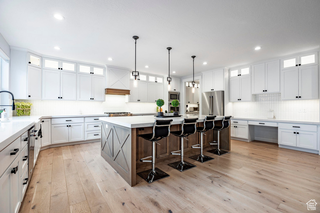 Kitchen with appliances with stainless steel finishes, a kitchen island, white cabinets, and light hardwood / wood-style flooring