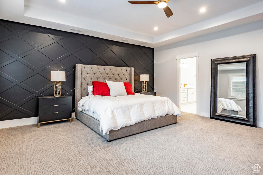 Bedroom with light carpet, a tray ceiling, connected bathroom, and ceiling fan