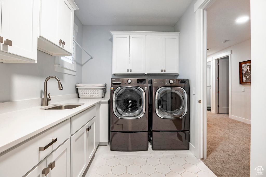 Laundry area with light tile flooring, sink, cabinets, and washer and clothes dryer