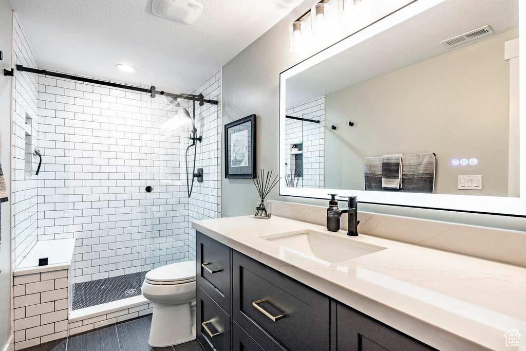 Bathroom featuring a textured ceiling, walk in shower, tile floors, vanity, and toilet