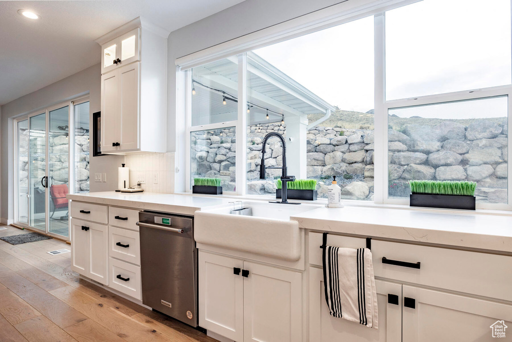 Kitchen with white cabinets, plenty of natural light, dishwasher, and light hardwood / wood-style floors