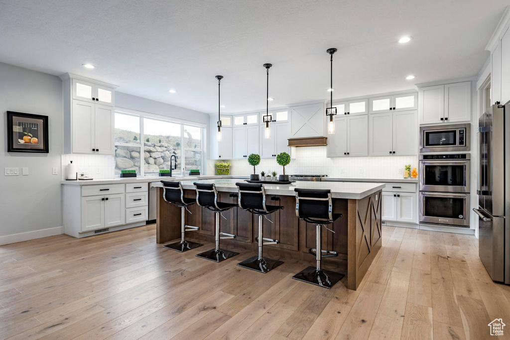 Kitchen featuring a kitchen island, light wood-type flooring, white cabinets, and appliances with stainless steel finishes