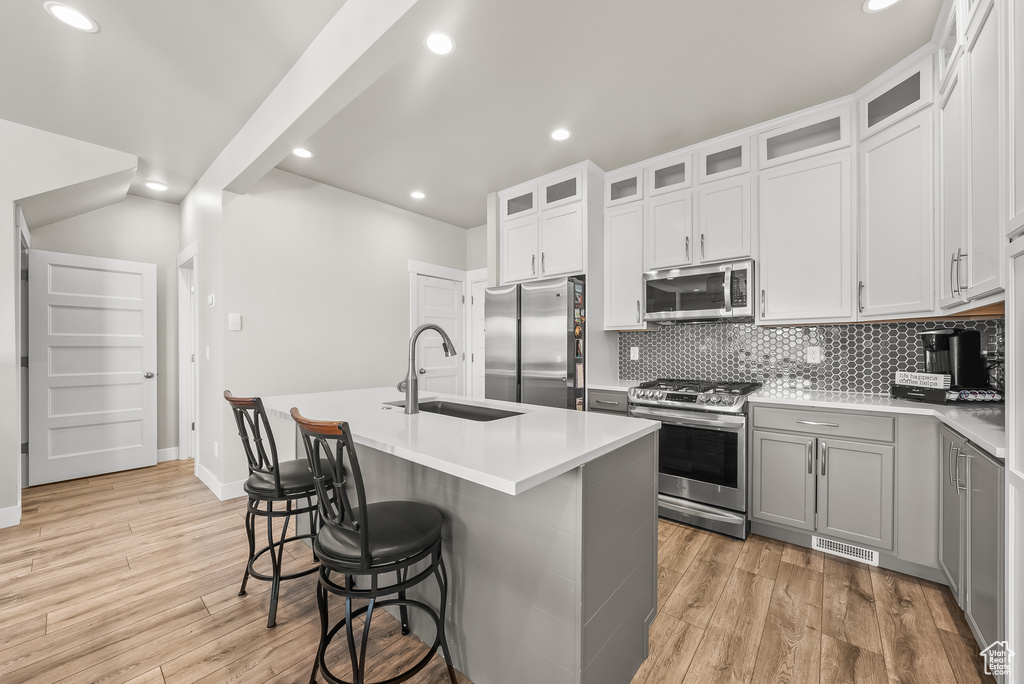 Kitchen with white cabinetry, sink, light hardwood / wood-style floors, a kitchen island with sink, and stainless steel appliances