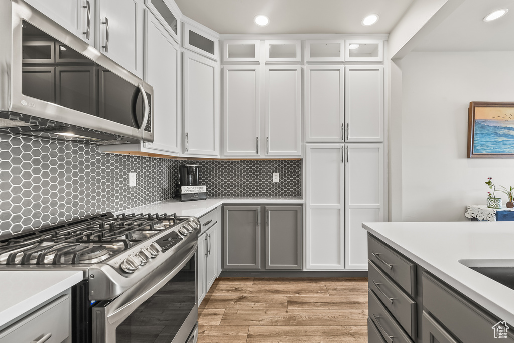Kitchen featuring appliances with stainless steel finishes, gray cabinets, white cabinets, and light hardwood / wood-style floors