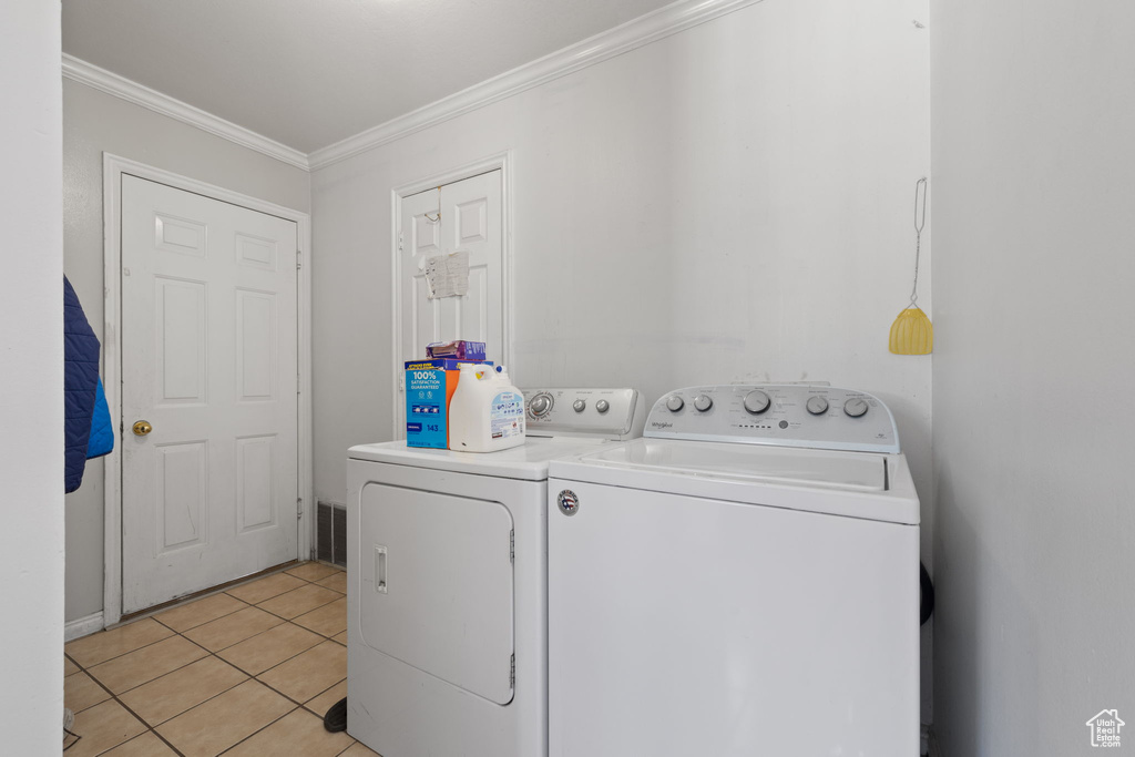 Laundry area featuring light tile floors, washer and dryer, and crown molding