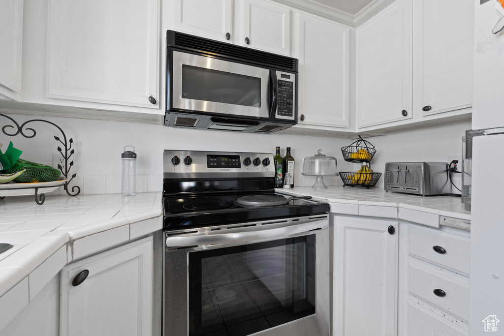Kitchen featuring tile counters, white cabinetry, and stainless steel appliances