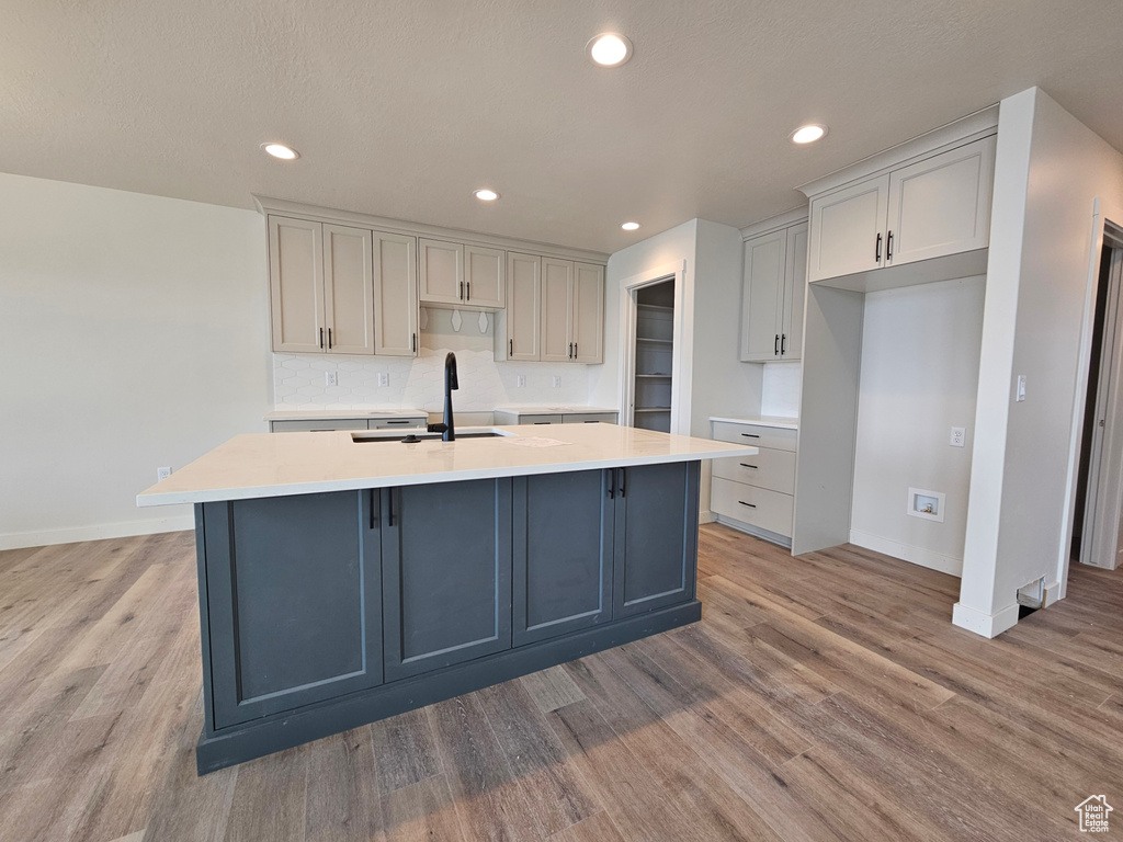 Kitchen with backsplash, light hardwood / wood-style flooring, sink, gray cabinets, and a kitchen island with sink