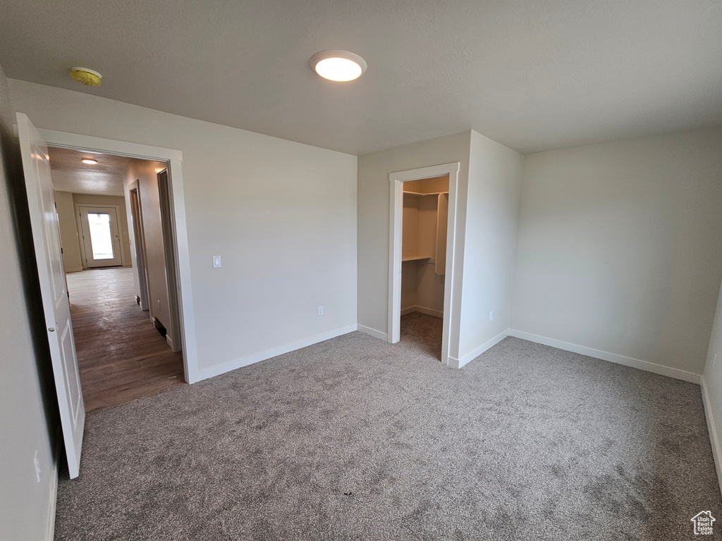 Unfurnished bedroom with dark carpet, a walk in closet, and a closet