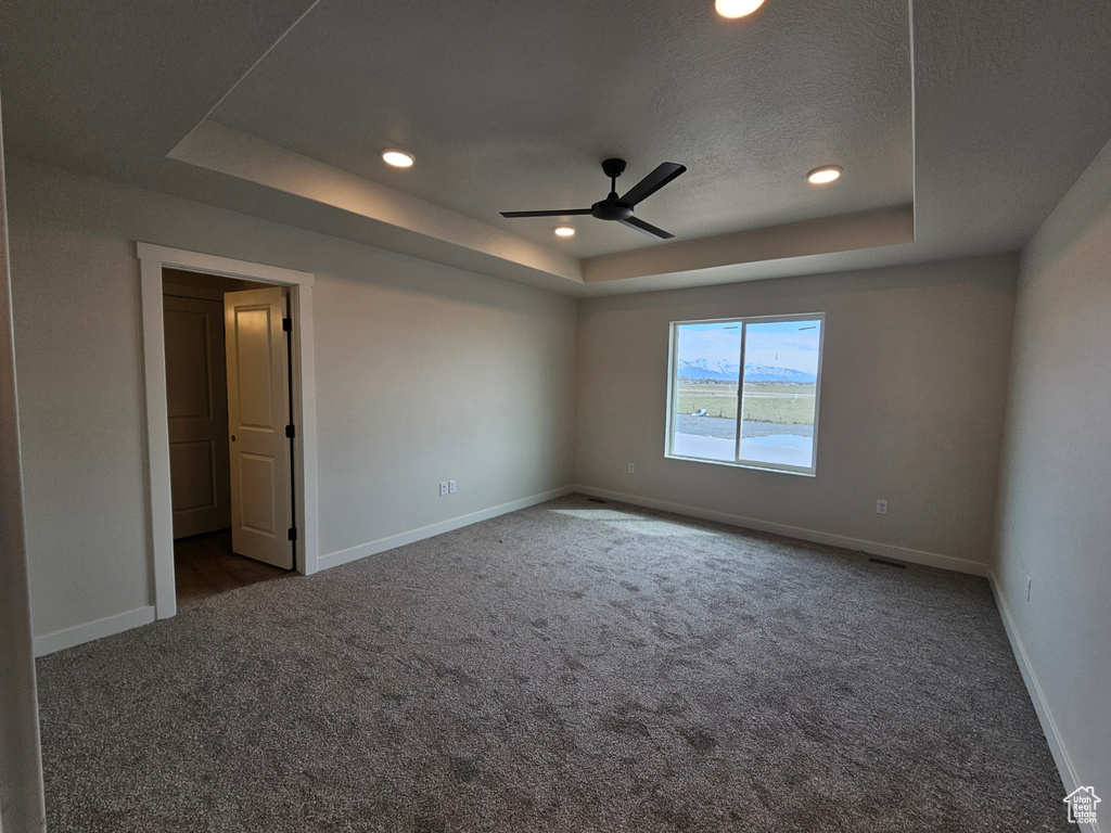 Empty room with dark carpet, ceiling fan, and a raised ceiling