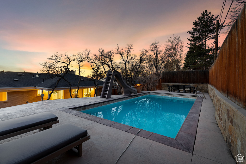 Pool at dusk with a patio area and a water slide