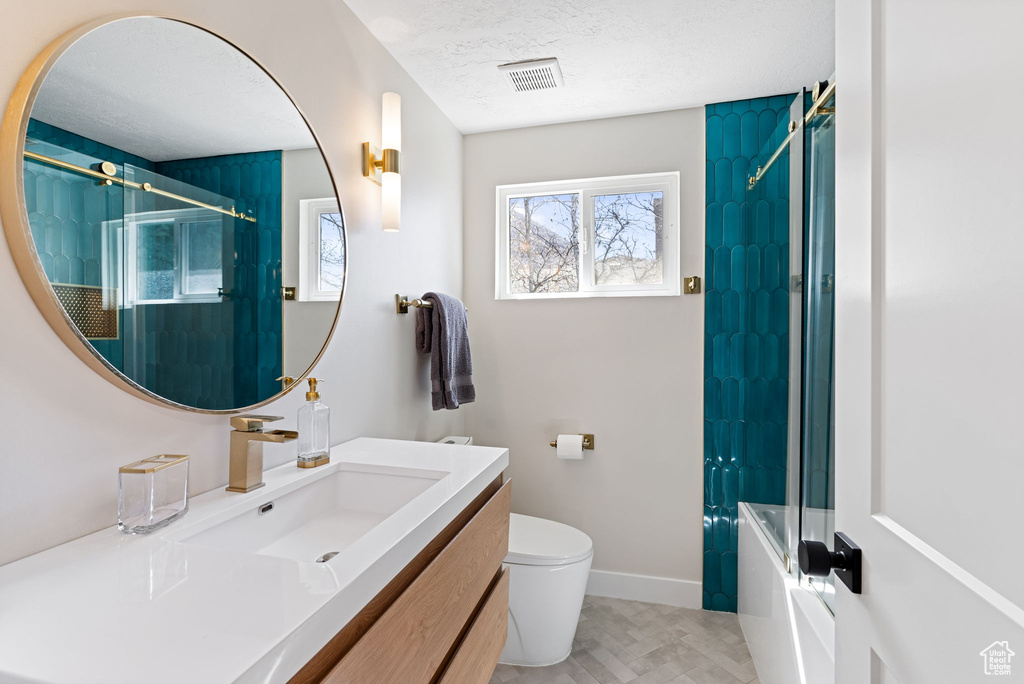 Full bathroom with a textured ceiling, large vanity, tile floors, combined bath / shower with glass door, and toilet