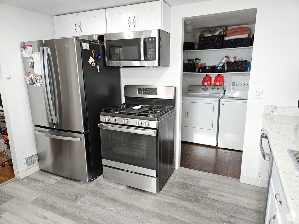 Kitchen featuring washer and clothes dryer, light stone countertops, appliances with stainless steel finishes, light hardwood / wood-style flooring, and white cabinets