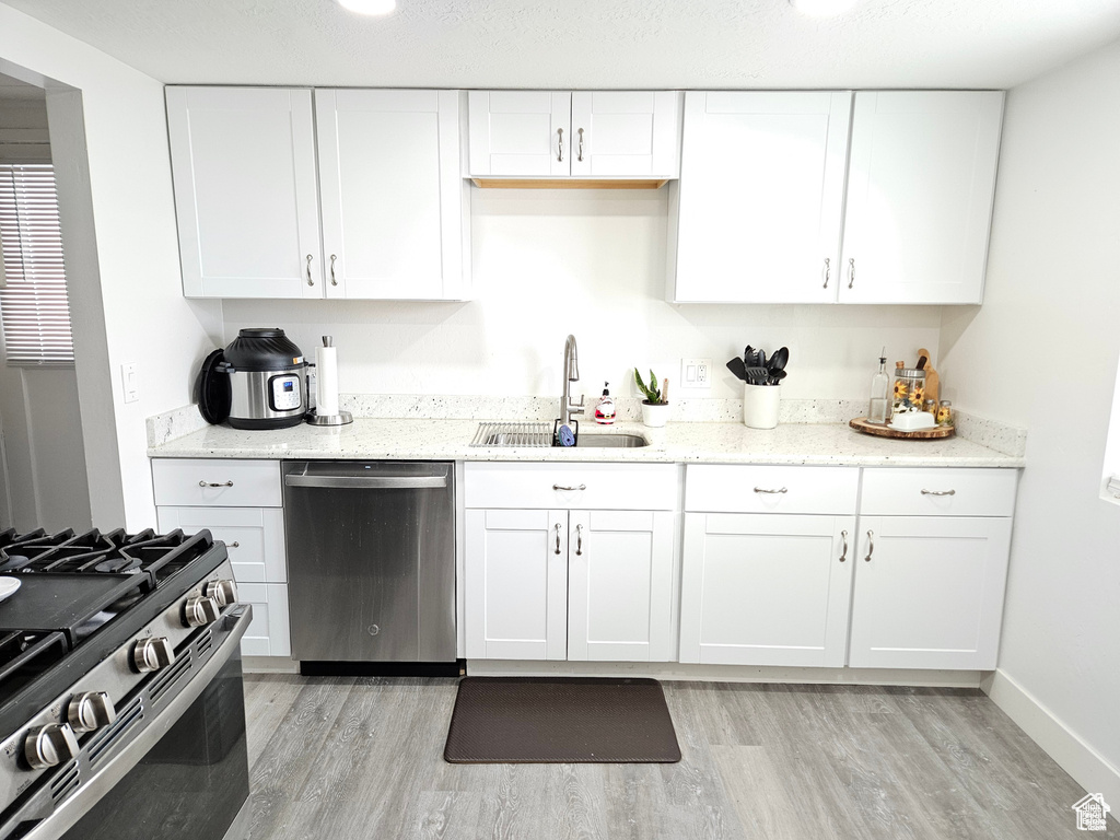 Kitchen with appliances with stainless steel finishes, white cabinetry, sink, and light hardwood / wood-style floors