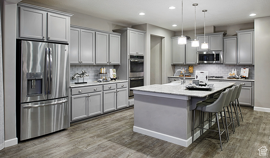Kitchen featuring appliances with stainless steel finishes, backsplash, pendant lighting, and dark wood-type flooring