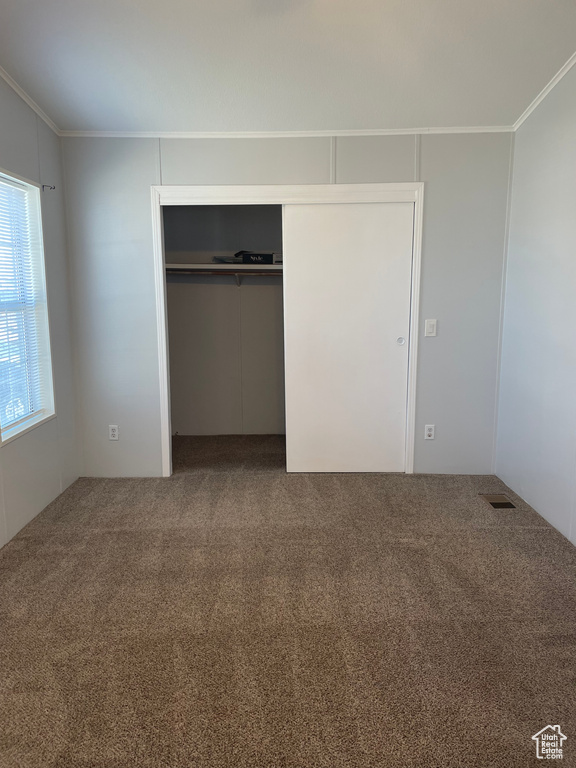 Unfurnished bedroom with dark colored carpet, a closet, and crown molding