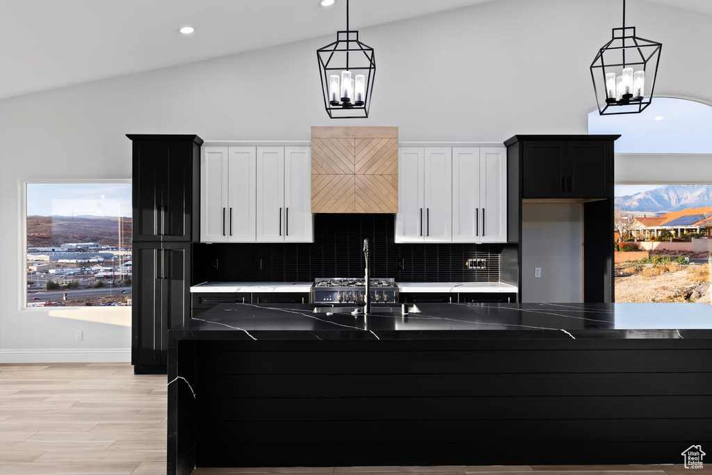 Kitchen with tasteful backsplash, light hardwood / wood-style floors, white cabinetry, an inviting chandelier, and pendant lighting