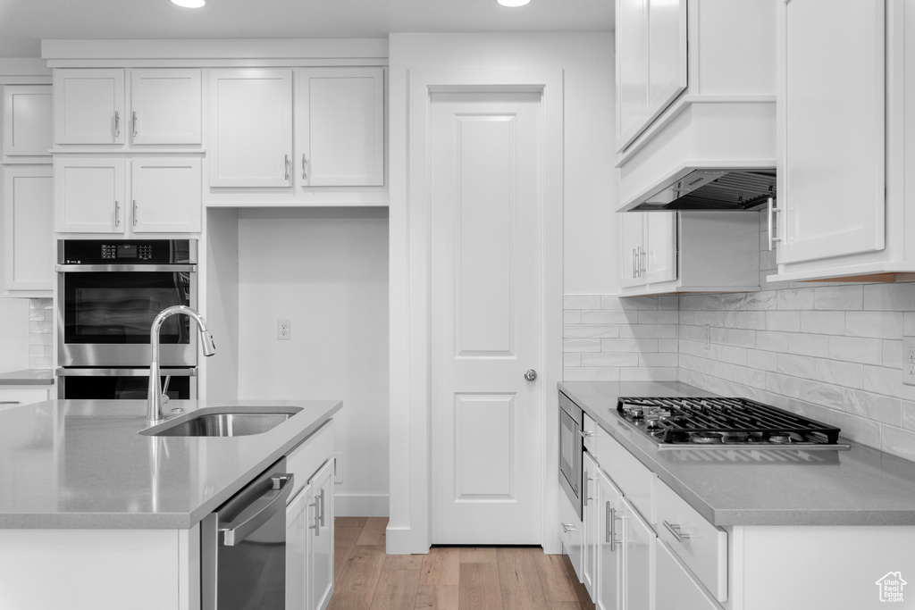 Kitchen with white cabinetry, sink, tasteful backsplash, appliances with stainless steel finishes, and light wood-type flooring