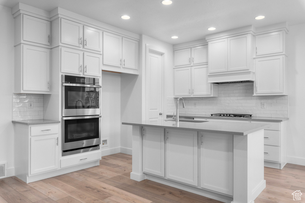Kitchen with backsplash, double oven, white cabinets, sink, and light wood-type flooring