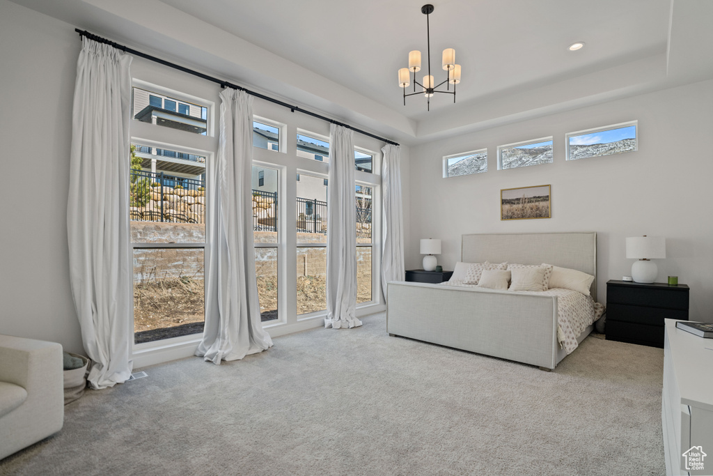 Carpeted bedroom featuring an inviting chandelier, a raised ceiling, and multiple windows