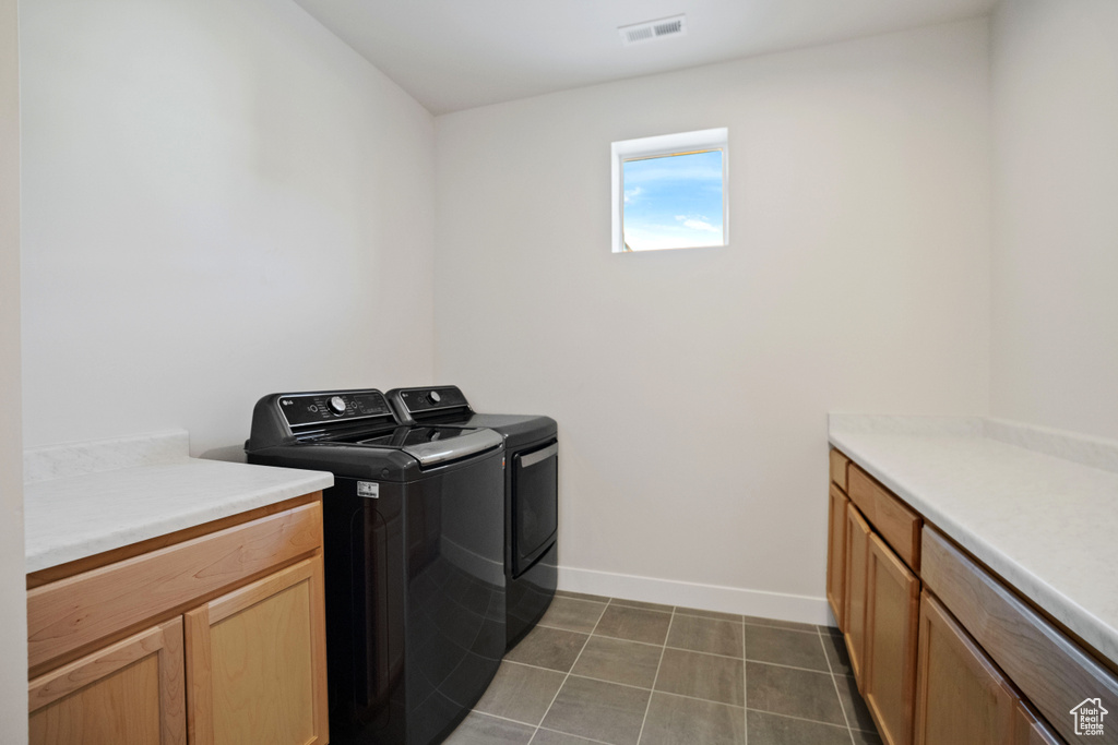 Laundry area with independent washer and dryer, cabinets, and dark tile flooring
