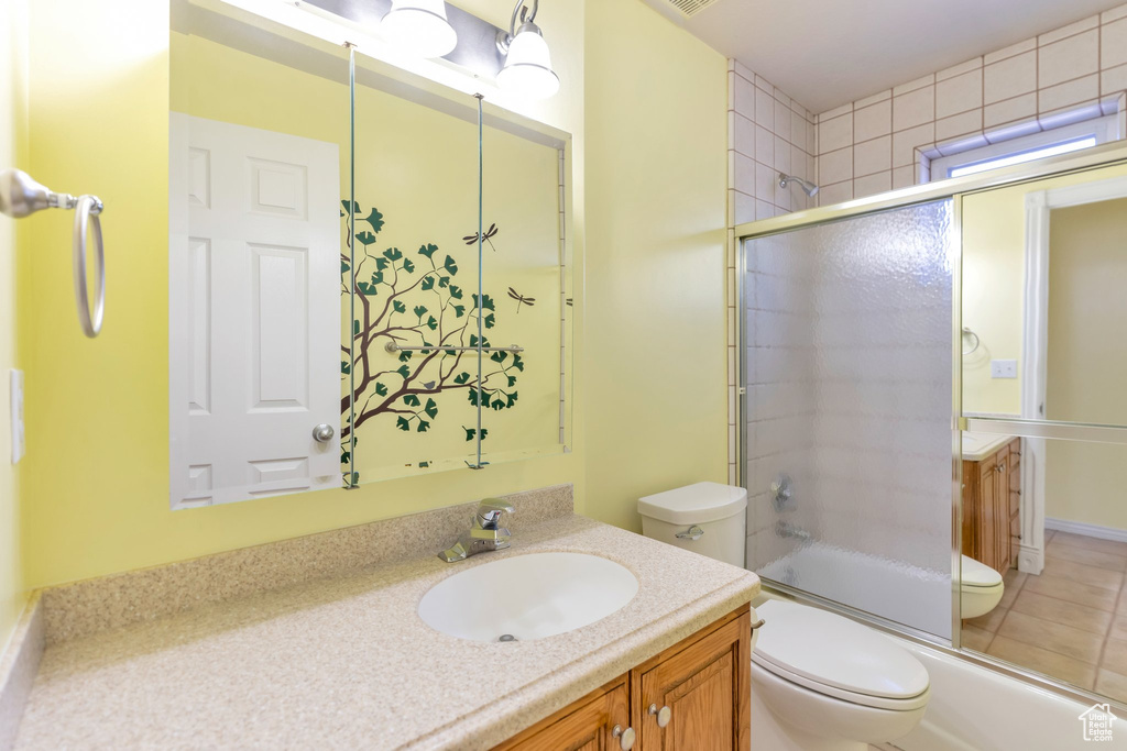 Full bathroom with tile floors, toilet, large vanity, and bath / shower combo with glass door