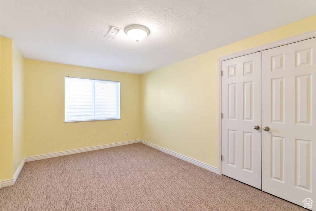 Unfurnished bedroom with a textured ceiling, a closet, and light colored carpet