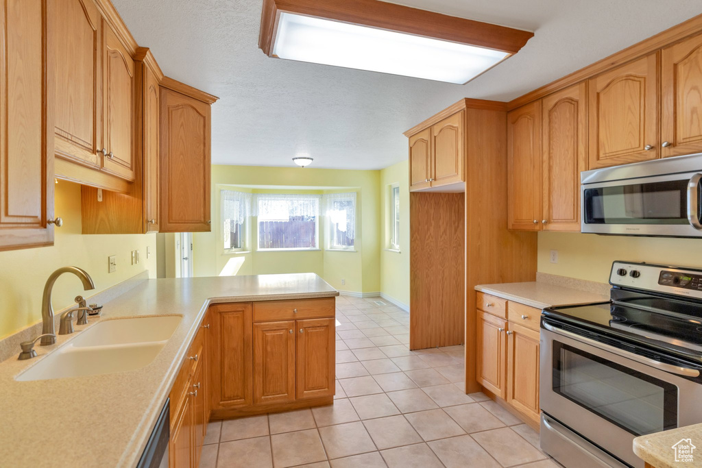 Kitchen featuring appliances with stainless steel finishes, kitchen peninsula, light tile floors, and sink