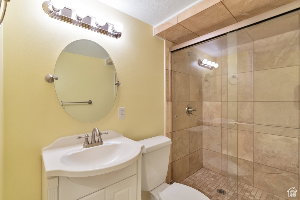 Bathroom featuring an enclosed shower, a textured ceiling, toilet, and vanity