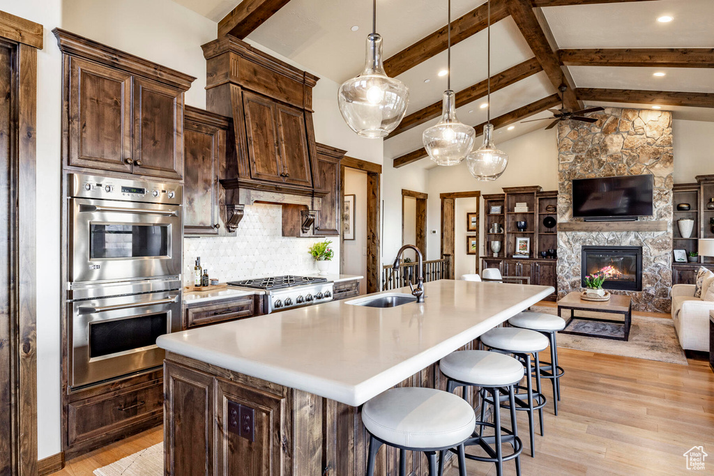 Kitchen with a stone fireplace, a kitchen island with sink, ceiling fan, and light hardwood / wood-style flooring