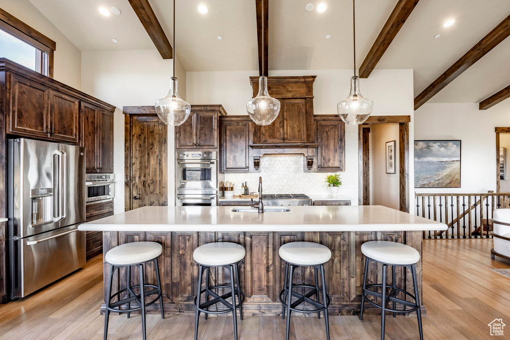 Kitchen with appliances with stainless steel finishes, a kitchen island with sink, light wood-type flooring, tasteful backsplash, and decorative light fixtures