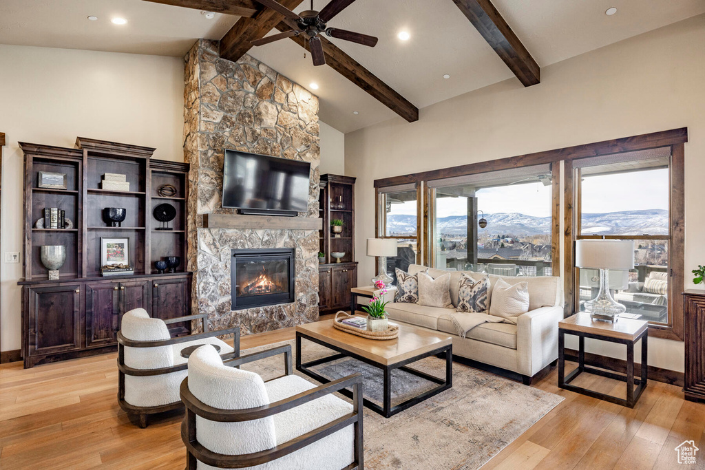 Living room featuring beam ceiling, a mountain view, ceiling fan, a stone fireplace, and light hardwood / wood-style floors