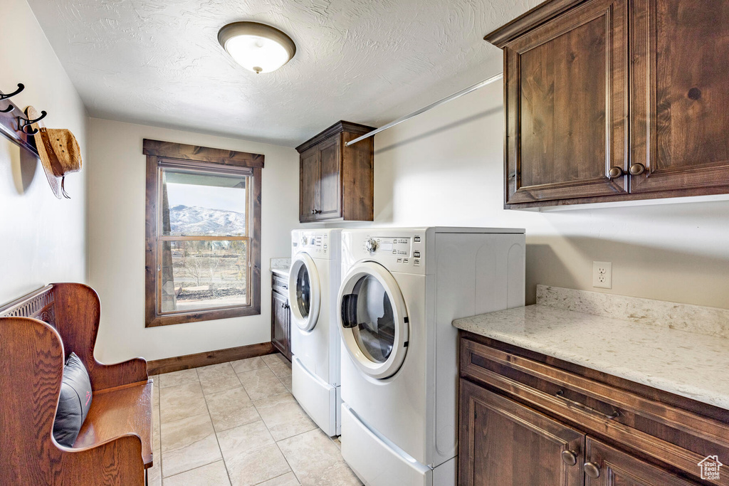 Laundry room featuring cabinets, a textured ceiling, light tile floors, and washer and dryer