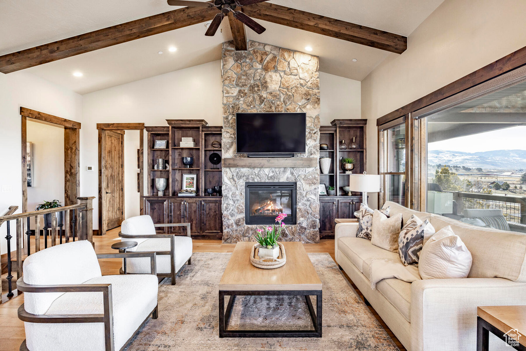 Living room featuring ceiling fan, high vaulted ceiling, light hardwood / wood-style floors, a fireplace, and beam ceiling