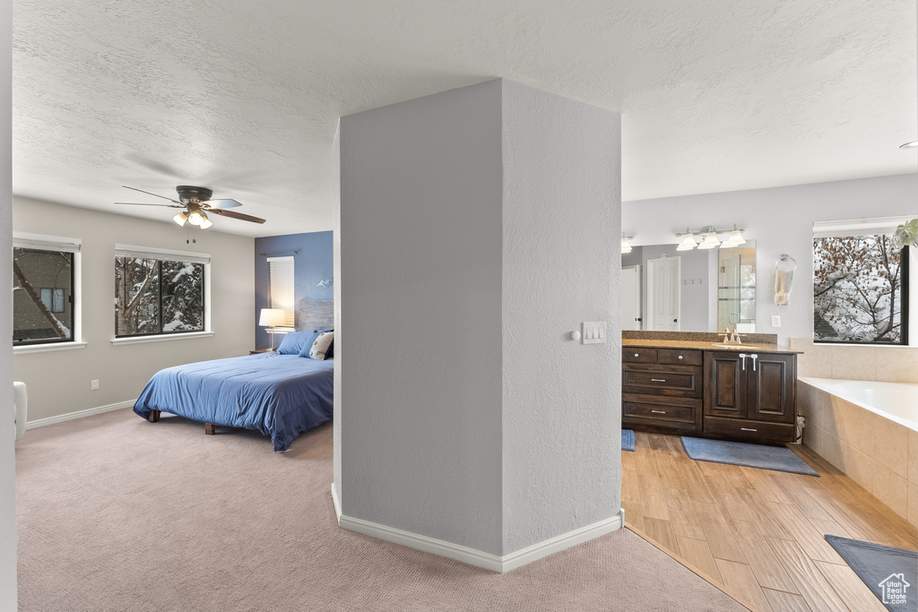 Bedroom with a textured ceiling, connected bathroom, ceiling fan, sink, and light wood-type flooring