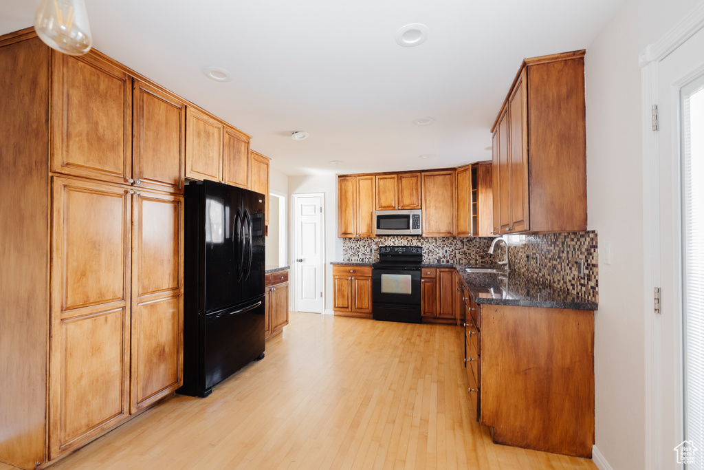 Kitchen featuring sink, dark stone counters, backsplash, black appliances, and light hardwood / wood-style flooring