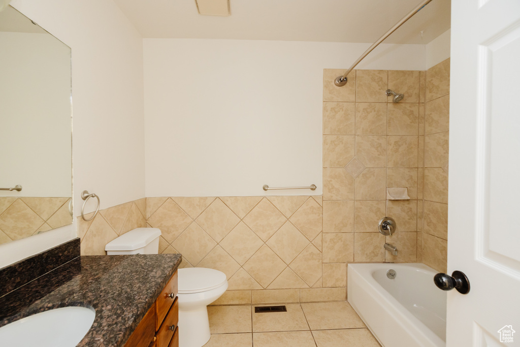 Full bathroom with vanity with extensive cabinet space, tiled shower / bath, tile walls, toilet, and tile floors