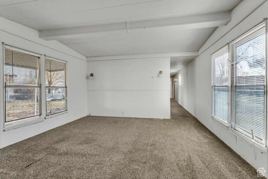 Empty room with lofted ceiling with beams, plenty of natural light, and carpet floors