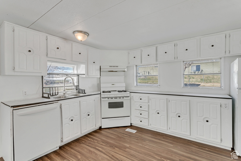 Kitchen featuring custom range hood, white cabinets, hardwood / wood-style floors, white appliances, and sink
