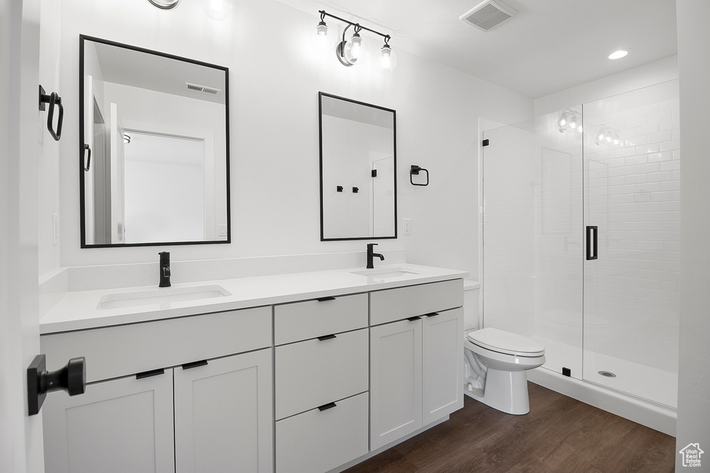 Bathroom with hardwood / wood-style flooring, dual sinks, a shower with shower door, vanity with extensive cabinet space, and toilet