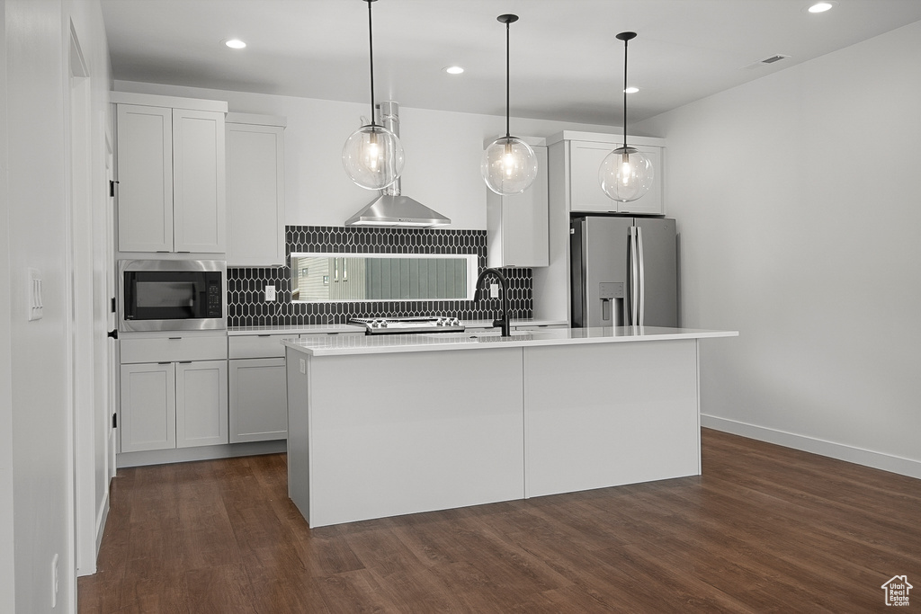 Kitchen with dark hardwood / wood-style flooring, appliances with stainless steel finishes, tasteful backsplash, and a center island with sink