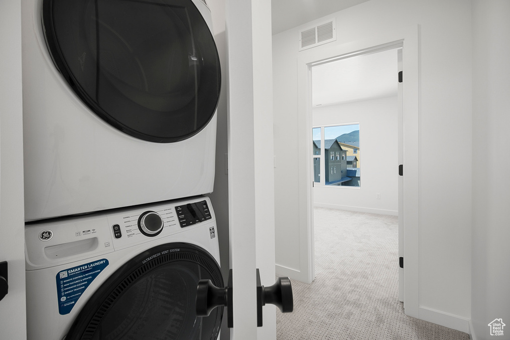 Washroom featuring stacked washer and clothes dryer and light carpet