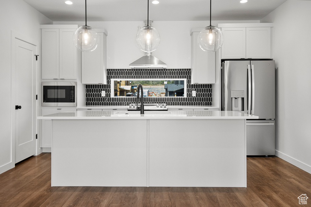 Kitchen with white cabinets, tasteful backsplash, a kitchen island with sink, and stainless steel fridge
