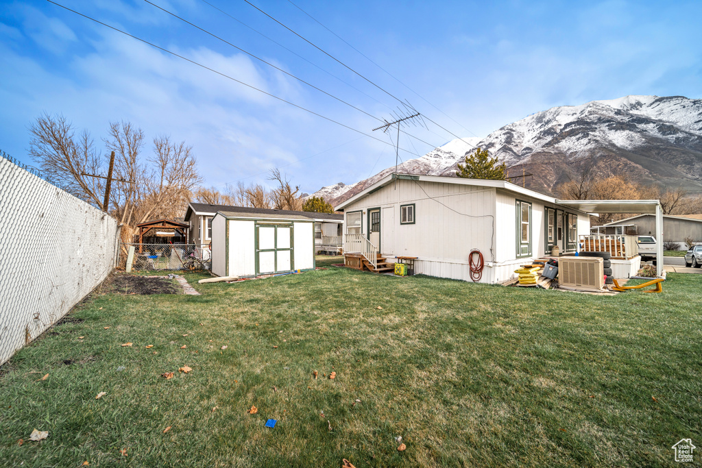 Rear view of property featuring a shed, a mountain view, a lawn, and central AC unit