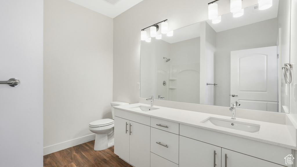 Bathroom featuring vanity with extensive cabinet space, dual sinks, hardwood / wood-style floors, and toilet