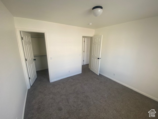 Unfurnished bedroom featuring dark colored carpet, a closet, and a walk in closet