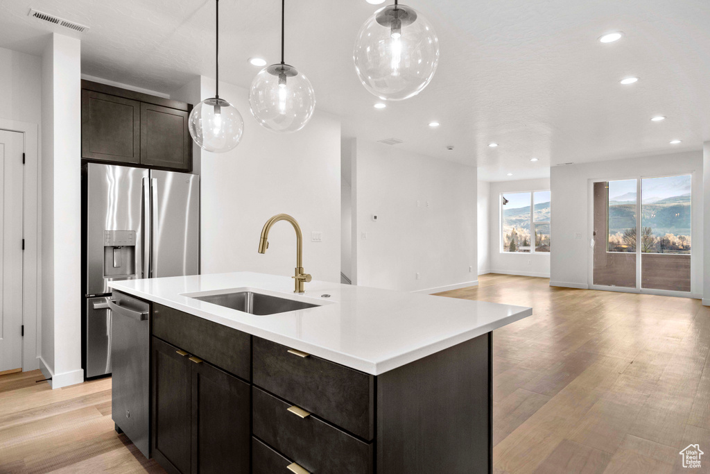 Kitchen with sink, pendant lighting, a center island with sink, light wood-type flooring, and dark brown cabinets