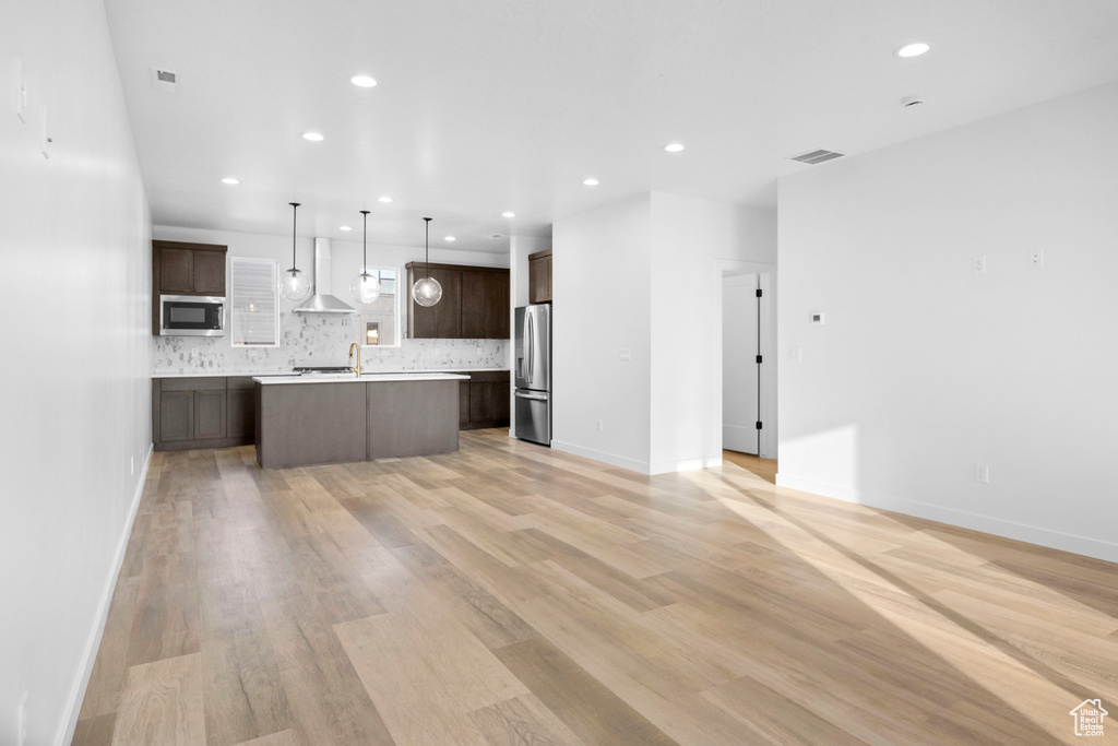 Kitchen featuring appliances with stainless steel finishes, hanging light fixtures, light hardwood / wood-style flooring, a kitchen island, and dark brown cabinets