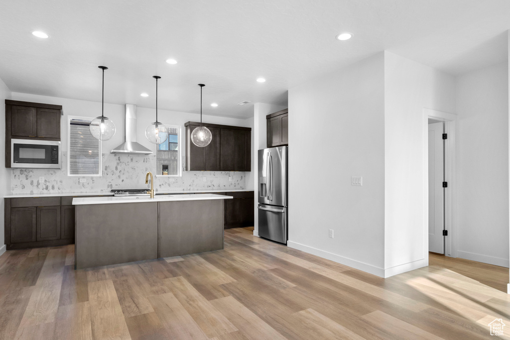 Kitchen featuring black microwave, stainless steel fridge, wall chimney exhaust hood, and light hardwood / wood-style floors