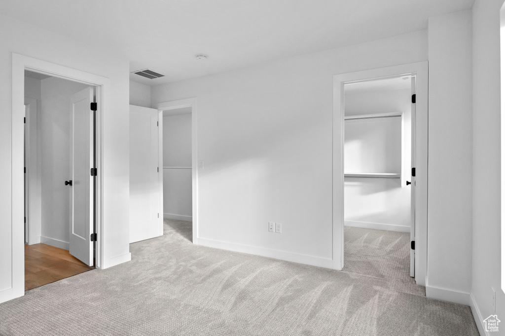 Unfurnished bedroom featuring a spacious closet, light colored carpet, and a closet